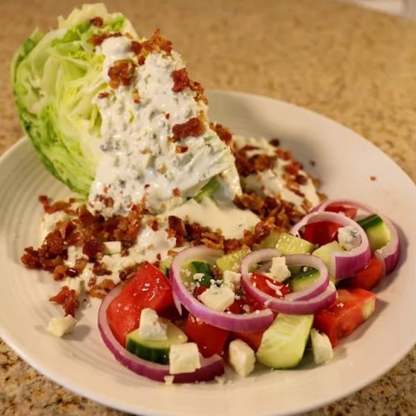 Wedge salad with blue cheese dressing, bacon, and a side of cucumber, tomato, and red onion.