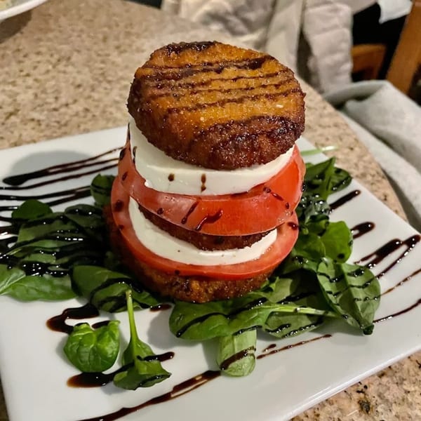 Stacked fried green tomatoes, fresh mozzarella, and sliced tomatoes, drizzled with balsamic glaze on spinach.