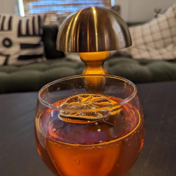 A fine-dining cocktail with a dried orange slice, next to a mushroom-shaped lamp.