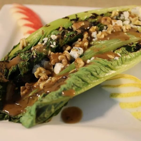 Grilled romaine lettuce with walnuts, blue cheese, and balsamic glaze, garnished with apple and pear slices.