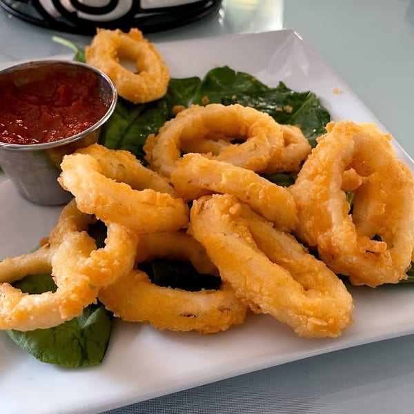 Golden-fried calamari rings with a side of red marinara sauce on a bed of green spinach.
