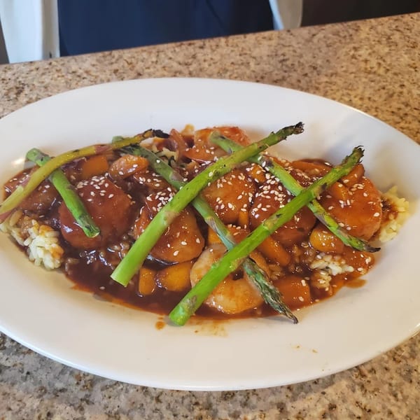 Sweet and sour chicken with asparagus and rice, garnished with sesame seeds on a white plate.