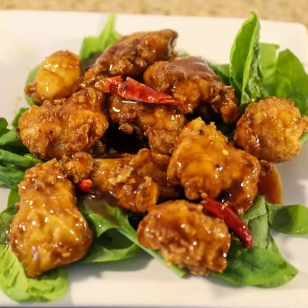 Windham Restaurant's crispy orange chicken with red chili peppers and fresh spinach on a white plate.