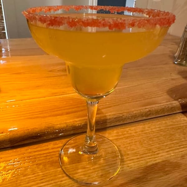A vibrant orange margarita with a red sugar-rimmed glass sits on a wooden table at Windham Restaurant.