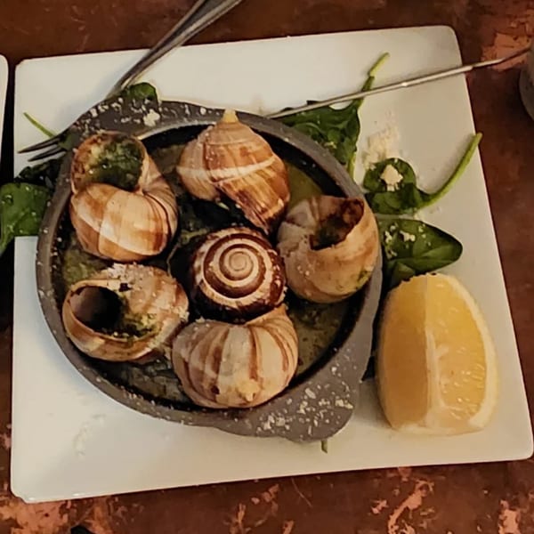 Escargots in shells with garlic butter, spinach, and a lemon wedge on a white plate.