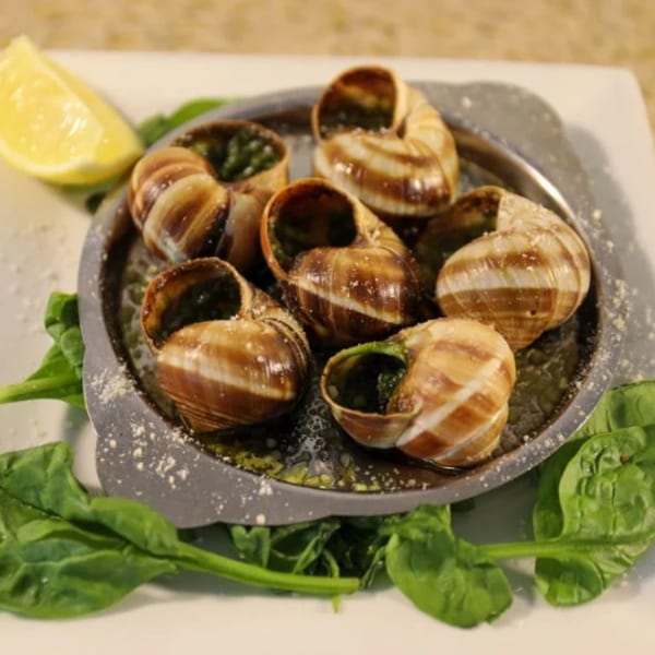 Escargots in shells with garlic butter, spinach, and a lemon wedge on a metal plate.
